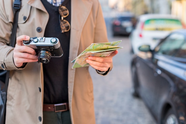 Photo gratuite un voyageur mâle tenant la carte et appareil photo vintage à la main
