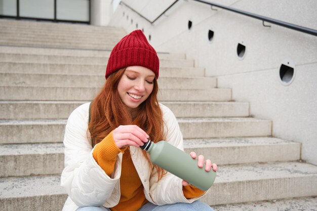 Photo gratuite voyageur souriant rousse touriste assise dans les escaliers avec une fiole boit du café chaud à partir d'un thermos