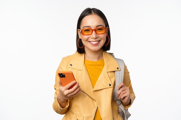 Voyageur Touristique élégant Jeune Femme Asiatique Avec Sac à Dos Et Smartphone Souriant à La Caméra Posant Sur Fond Blanc