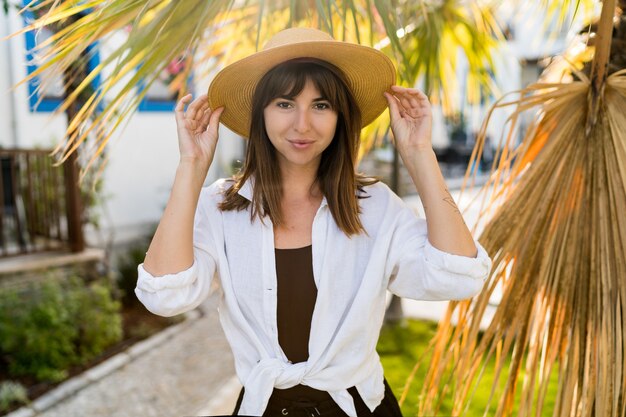 Vportrait d'été de jolie femme brune en chapeau de paille posant en plein air.