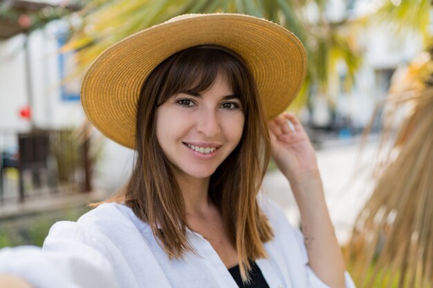 Vportrait d'été de jolie femme brune en chapeau de paille posant en plein air.