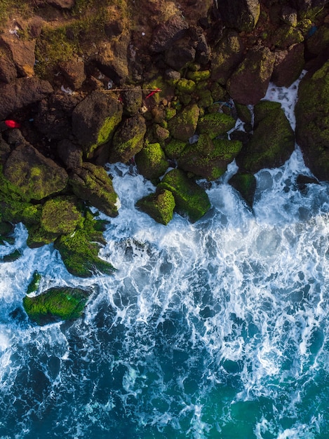 Vue aérienne aérienne verticale d'une mer bleue ondulée contre les rochers