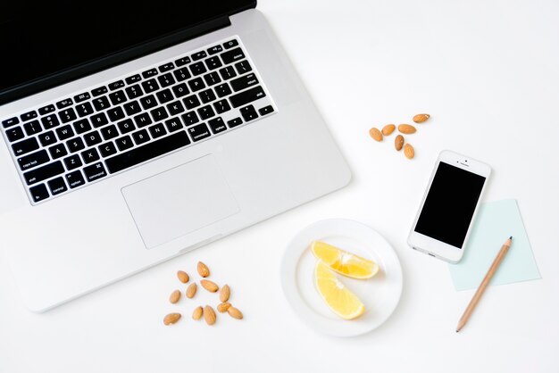 Vue aérienne des amandes; citron doux; crayon; smartphone et ordinateur portable sur un bureau blanc