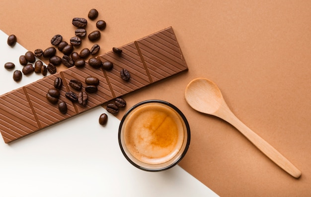Photo gratuite une vue aérienne de la barre de chocolat; grains de café torréfiés avec verre à café et cuillère