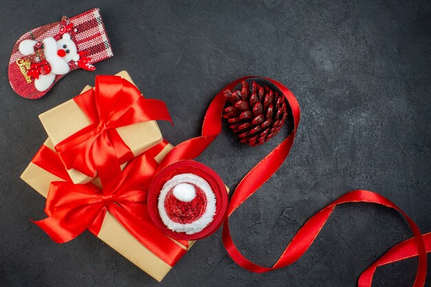 Vue aérienne de beaux cadeaux avec ruban rouge et chapeau de père Noël conifère chaussette de Noël sur table sombre