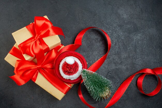 Vue aérienne de beaux cadeaux avec ruban rouge et sapin de Noël chapeau de père Noël sur table sombre