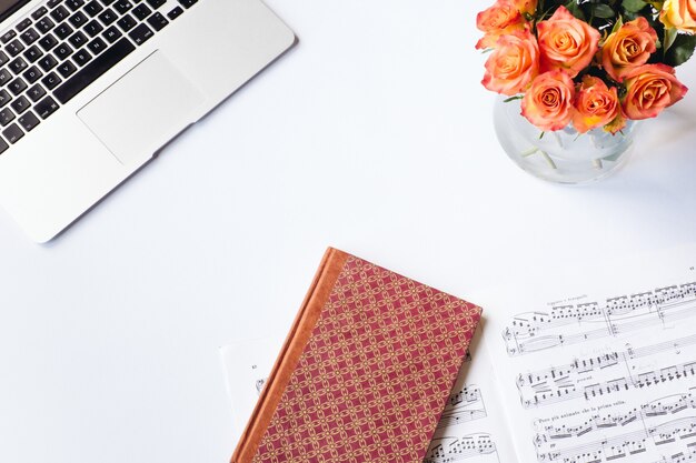 Vue aérienne d'un bureau blanc avec un cahier rouge des fleurs une feuille de musique et un ordinateur portable