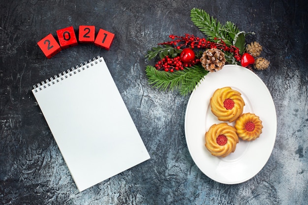 Vue aérienne de délicieux biscuits sur une assiette blanche et décorations du nouvel an numéros de chapeau de père noël prochain cahier sur une surface sombre