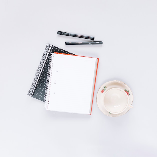 Photo gratuite vue aérienne de deux cahiers à spirale; stylo et tasse vide sur fond blanc