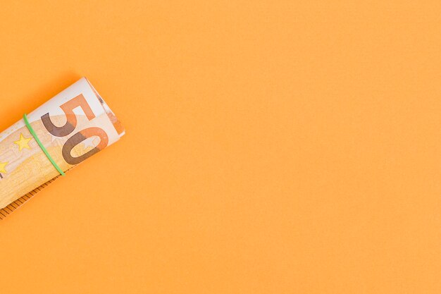 Une vue aérienne du billet en euros retroussé attaché avec du caoutchouc sur un fond orange