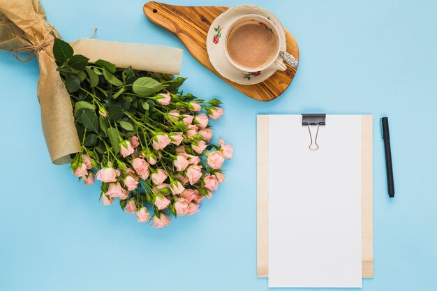 Une vue aérienne du bouquet de fleurs; tasse à café; presse-papier et stylo sur fond bleu