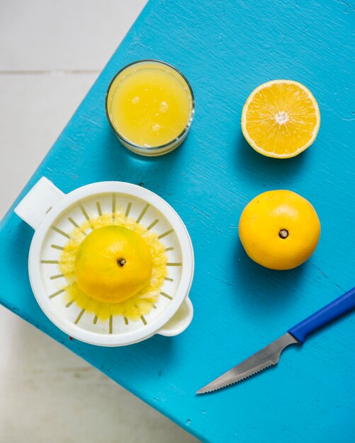 Vue aérienne du jus de citron vert avec un presse-agrumes manuel sur un bureau bleu