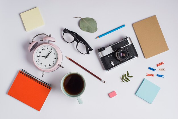 Une vue aérienne du réveil; lunettes; caméra; tasse à café et fournitures de bureau sur fond blanc