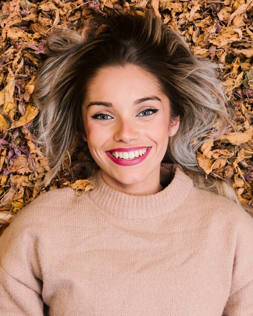 Vue aérienne de femme souriante allongée sur des feuilles sèches, regardant la caméra