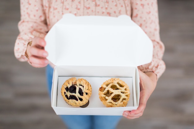 Photo gratuite vue aérienne d'une femme tenant une boîte blanche contenant deux petites pâtisseries