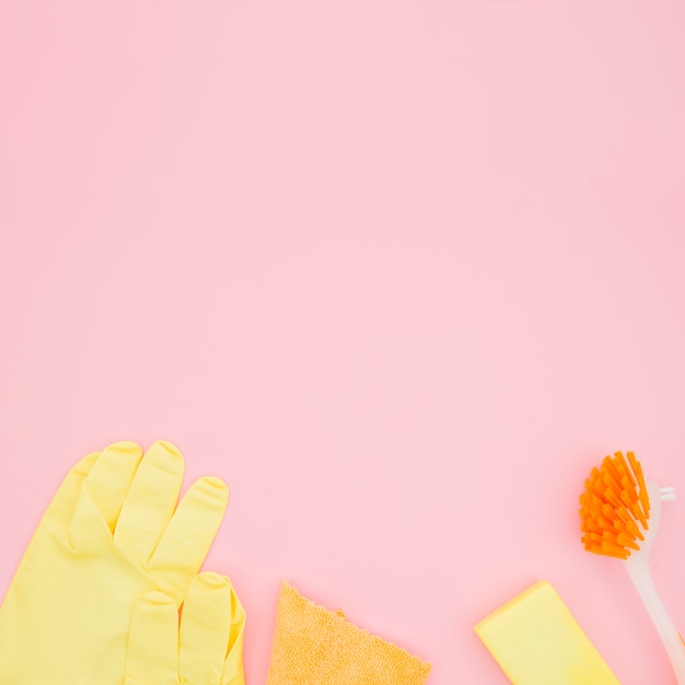 Une vue aérienne de gants; brosse; éponge et bouteille sur fond rose