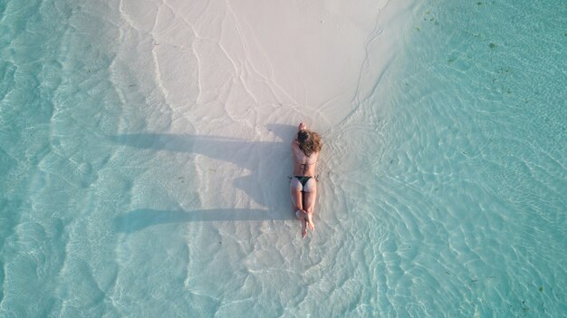 Vue aérienne d'une jeune fille allongée sur le sable et bronzage à la plage