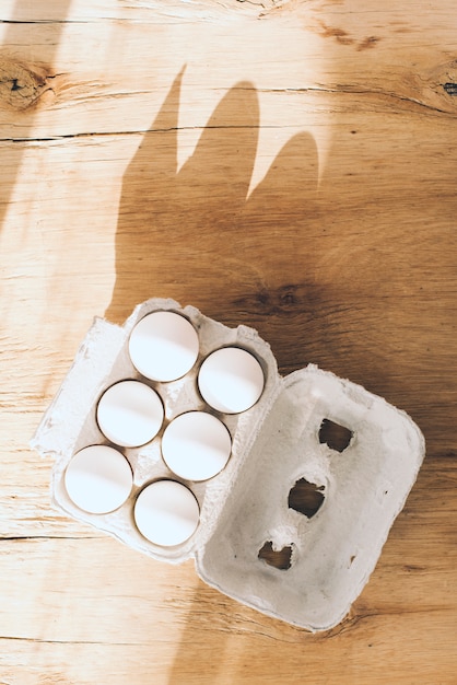 Une vue aérienne de la lumière du soleil qui tombe sur le carton d&#39;oeufs blancs sur un fond en bois