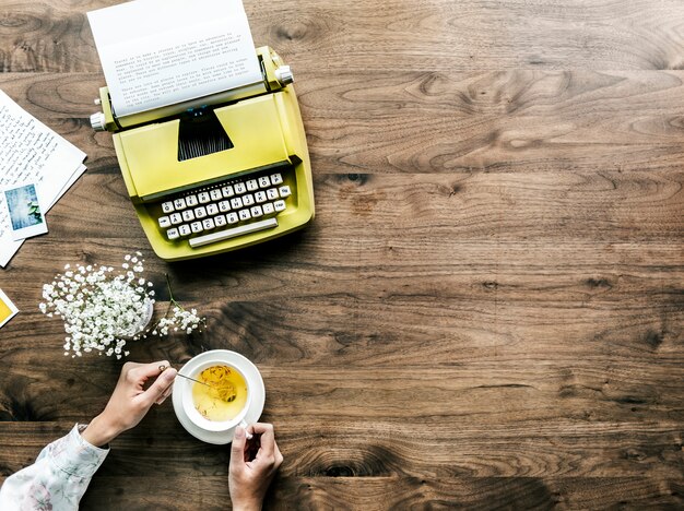 Vue aérienne d&#39;une machine à écrire rétro et d&#39;une femme avec une tasse de thé