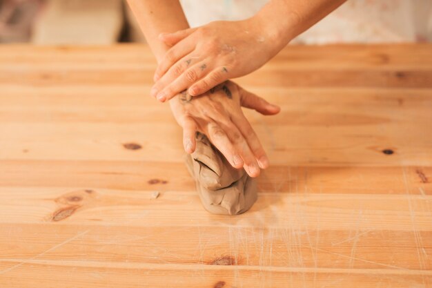 Une vue aérienne des mains de la femme sur l&#39;argile malaxée sur une table en bois