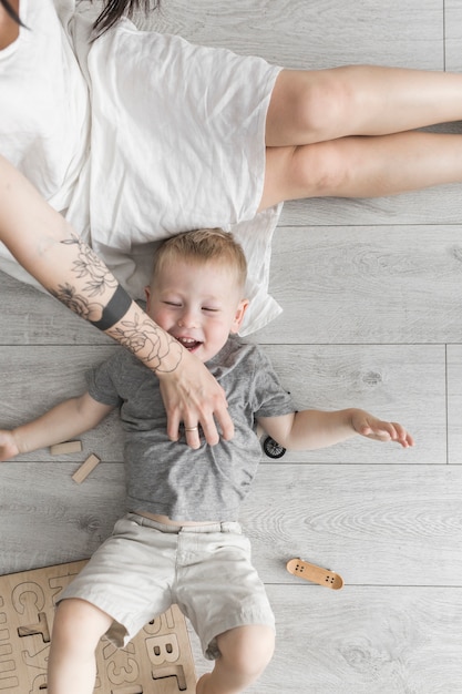 Vue aérienne de la mère chatouillant son fils allongé sur un plancher de bois franc