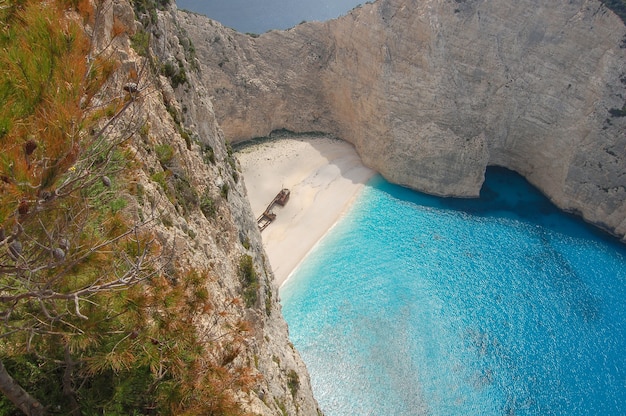 Vue aérienne de l'océan bleu entouré de falaises avec les restes d'un vieux bateau sur la rive