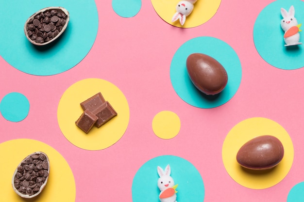 Photo gratuite une vue aérienne des oeufs de pâques; chips de lapin et choco sur cadre rond sur fond rose