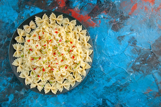 Vue aérienne de pâtes farfalle italiennes crues avec des légumes sur le côté droit sur fond bleu