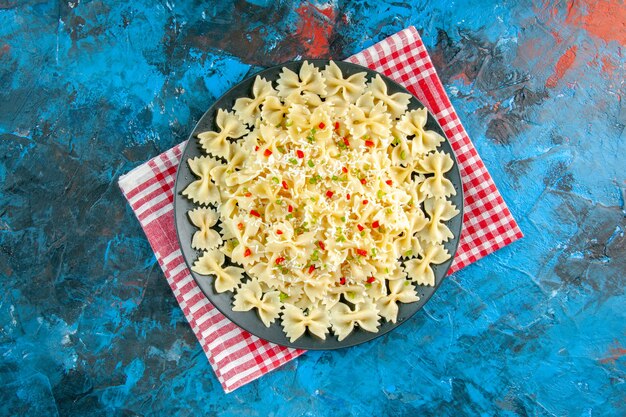 Vue aérienne de pâtes farfalle italiennes crues sur une serviette dénudée rouge sur une table bleue