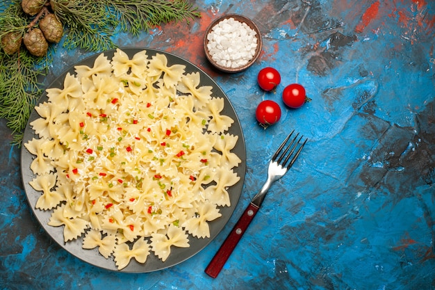 Photo gratuite vue aérienne de pâtes farfalle avec légumes tomates sel et branches de sapin fourche sur fond bleu