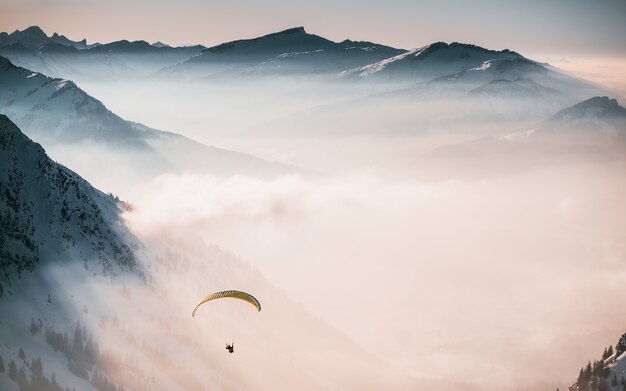 Vue aérienne d'une personne qui descend en parachute au-dessus des nuages près des montagnes enneigées