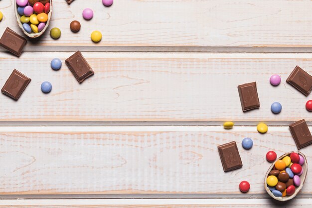 Une vue aérienne de pierres précieuses colorées et de morceaux de chocolat sur un bureau en bois