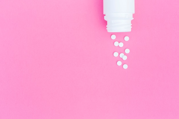 Une vue aérienne de pilules rondes blanches renversées de la bouteille sur fond rose