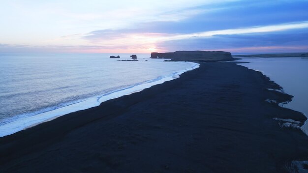 Vue aérienne de la plage de sable noir avec des montagnes et de grandes pierres en Islande, magnifique paysage naturel sur la plage Reynisfjara. Paysage islandais avec l'océan Atlantique sur la côte. Motion lente.