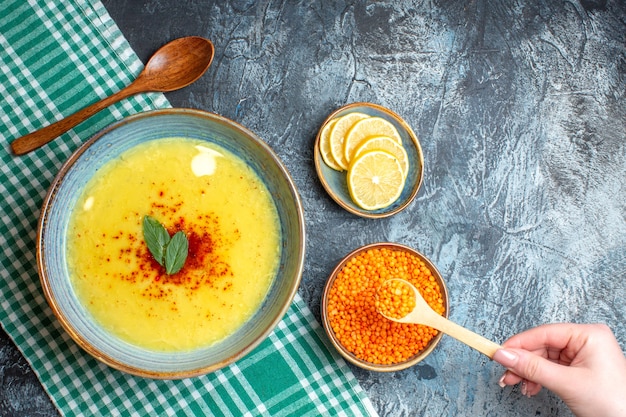 Photo gratuite vue aérienne d'un pot bleu avec une soupe savoureuse servie avec de la menthe et du poivre à côté d'une cuillère en bois de citron haché et d'un pois jaune sur fond bleu