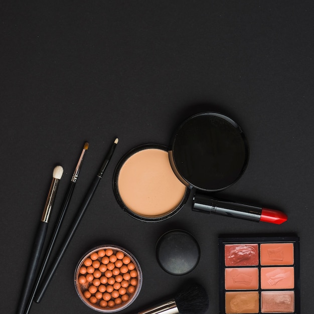 Vue aérienne des produits de maquillage avec des brosses sur fond noir