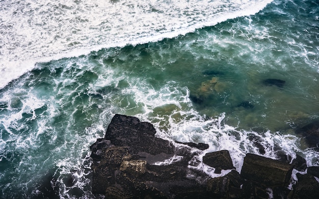 Vue aérienne d'un rivage rocheux près d'un plan d'eau avec des rochers éclaboussant les rochers