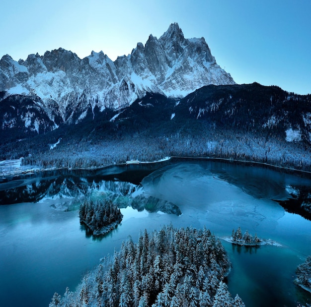 Photo gratuite vue aérienne de la rivière eibsee gelée entourée d'arbres couverts de neige en bavière, allemagne