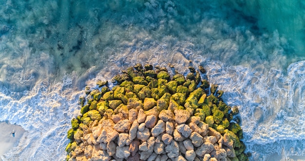 Vue aérienne des rochers les uns sur les autres entourés par la mer ondulée sous la lumière du soleil pendant la journée