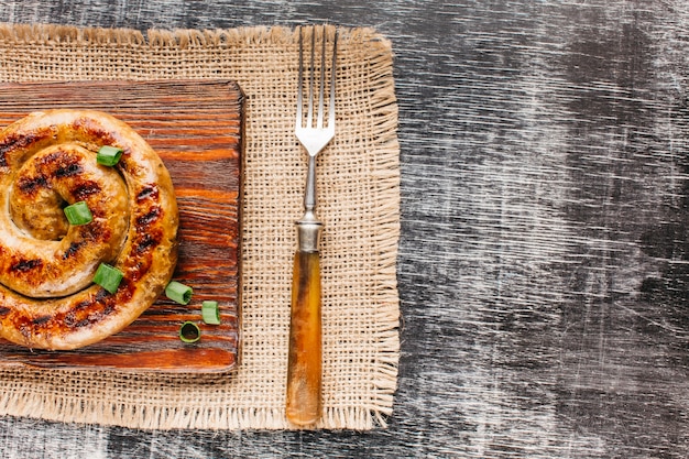 Vue aérienne de saucisse en spirale grillée avec échalote sur une planche à découper sur fond texturé en bois