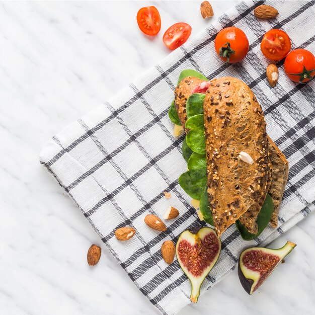 Vue aérienne d&#39;un savoureux hot-dog; amandes; tranches de figues fraîches et tomates cerises sur la serviette sur fond blanc