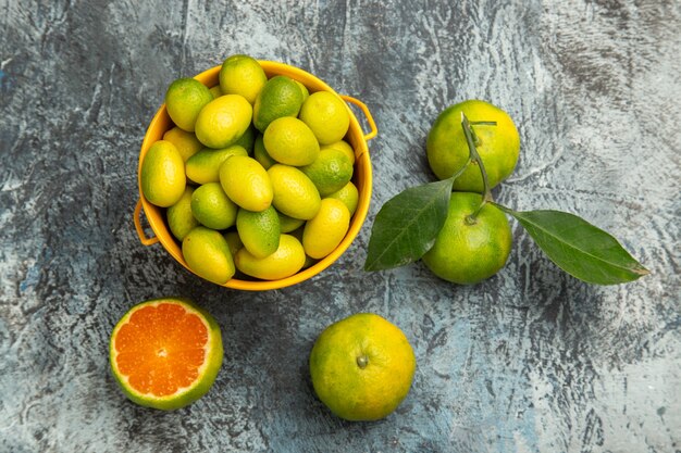 Vue aérienne d'un seau jaune plein de mandarines vertes fraîches et coupées en deux mandarines sur fond gris