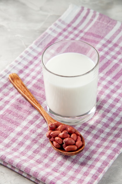 Photo gratuite vue aérienne d'une tasse en verre remplie de lait et d'arachides en cuillère sur une serviette dénudée violette