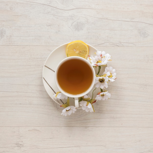 Photo gratuite vue aérienne de thé au citron dans une tasse avec des fleurs et citron sur une soucoupe