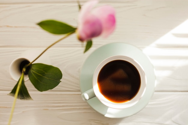 Vue aérienne de vase à fleur et café noir sur une table en bois blanche