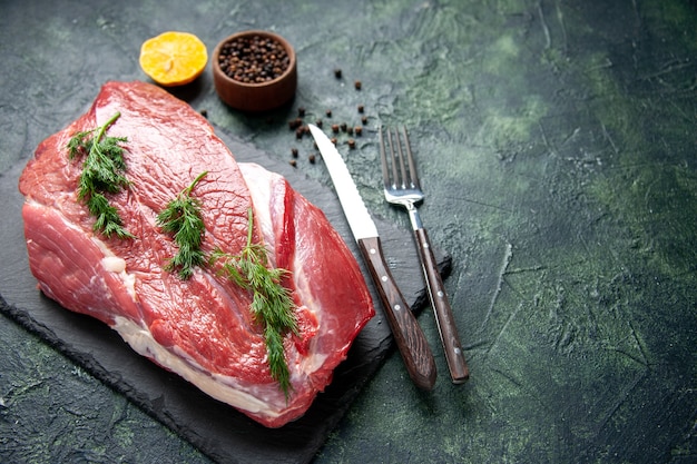 Vue aérienne de vert sur des couverts de viande crue rouge frais sur une planche à découper et du poivre citron sur fond de couleur vert noir mélangé