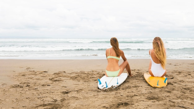 Vue arrière des amies à la plage avec des planches de surf