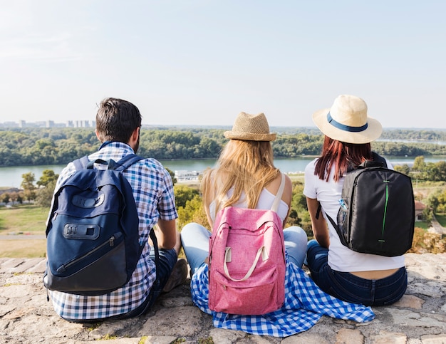 Photo gratuite vue arrière d'amis avec sac à dos assis à l'extérieur