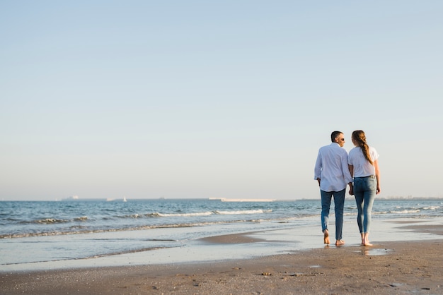 Vue arrière du couple marchant sur la plage de sable fin