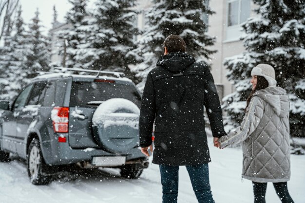 Vue arrière du couple profitant de la neige lors d'un road trip avec voiture